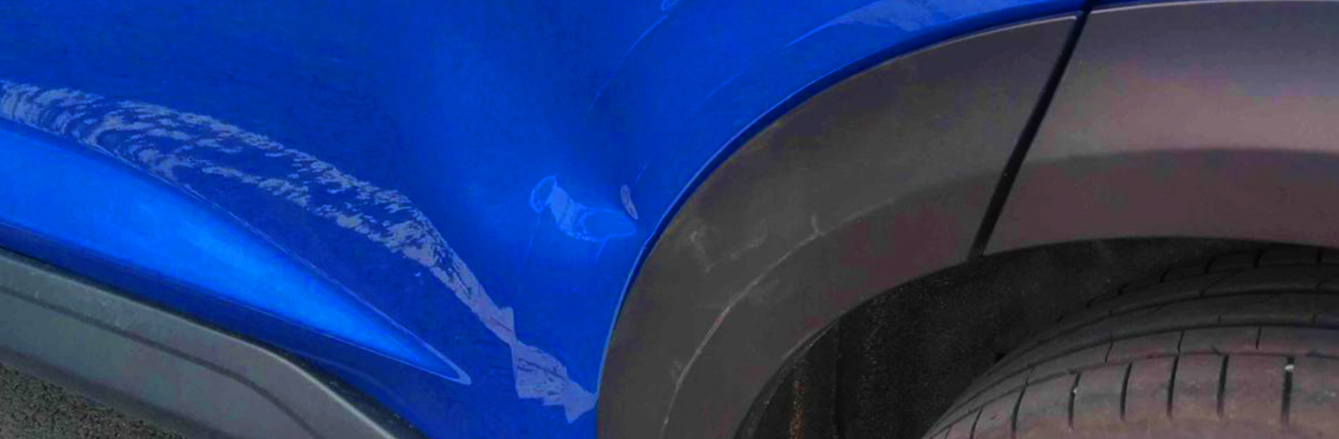 An image of a small dent on the side of a blue car.