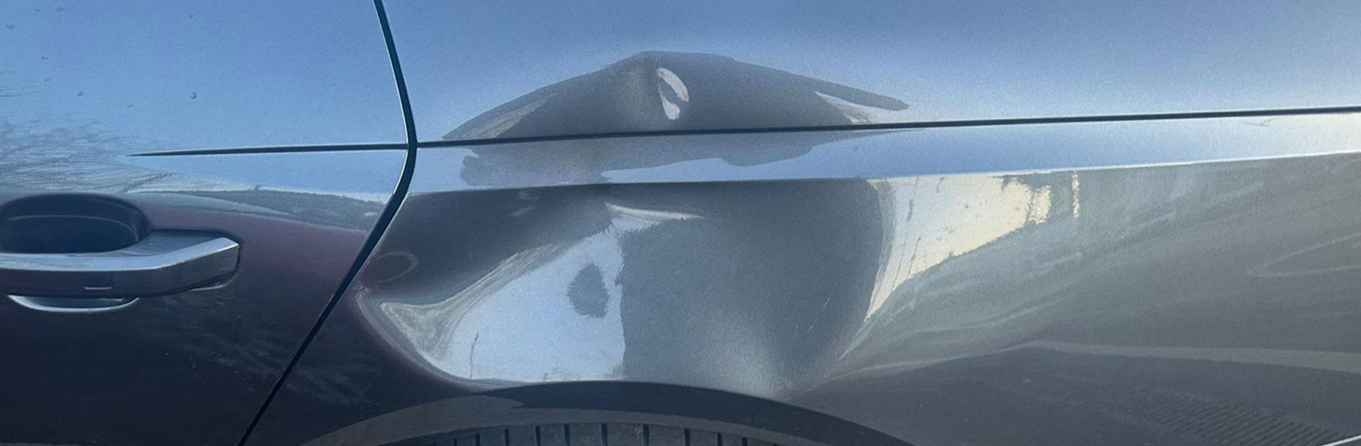 An image of a large dent on the side of a silver car.