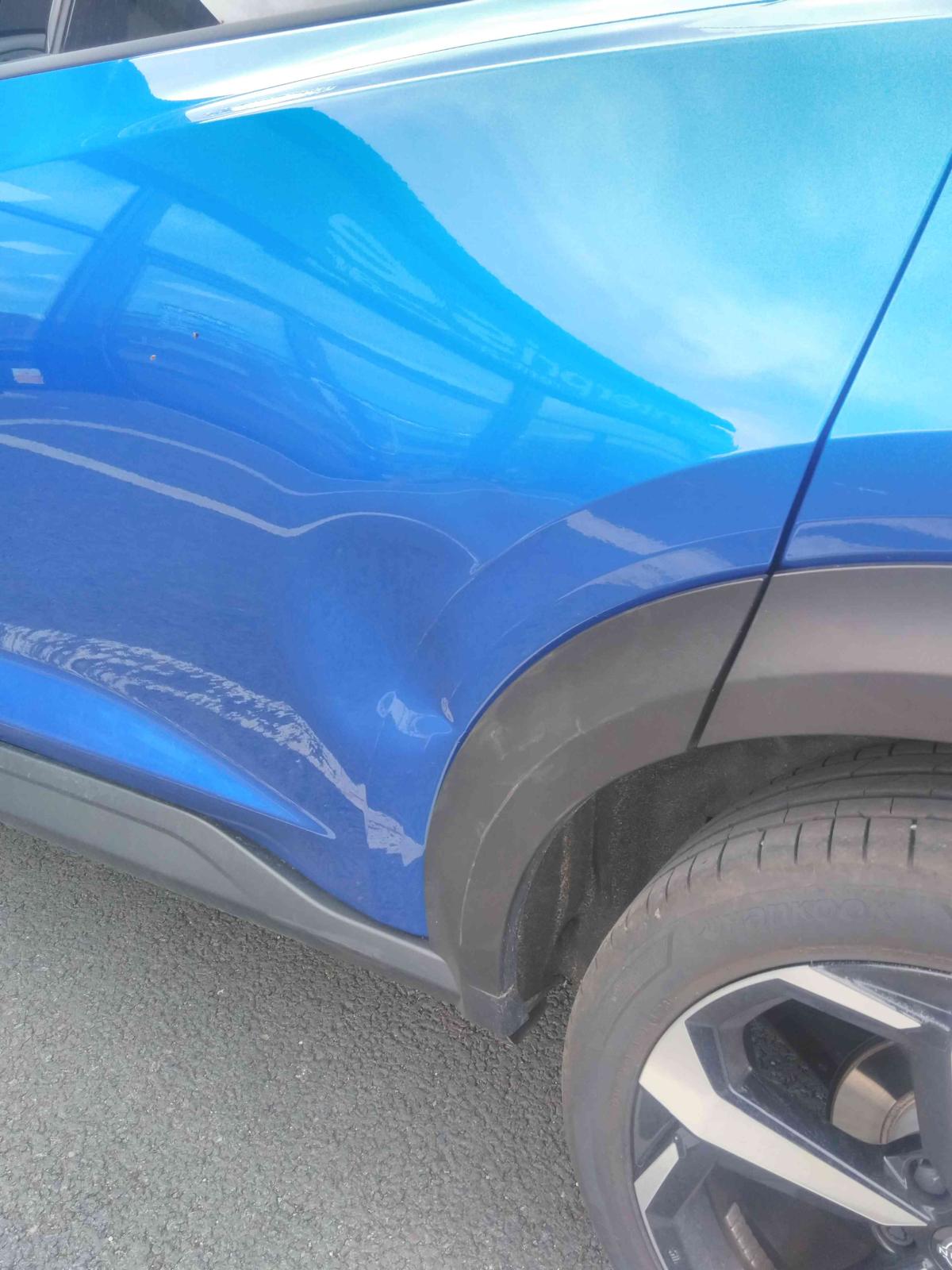 A dent in a royal blue Nissan.